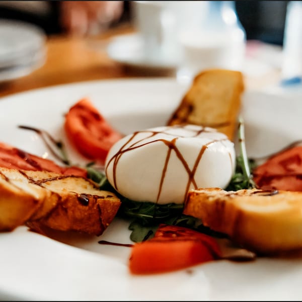 A burrata cheese ball drizzled with balsamic glaze, served with tomatoes, arugula, and toasted bread.