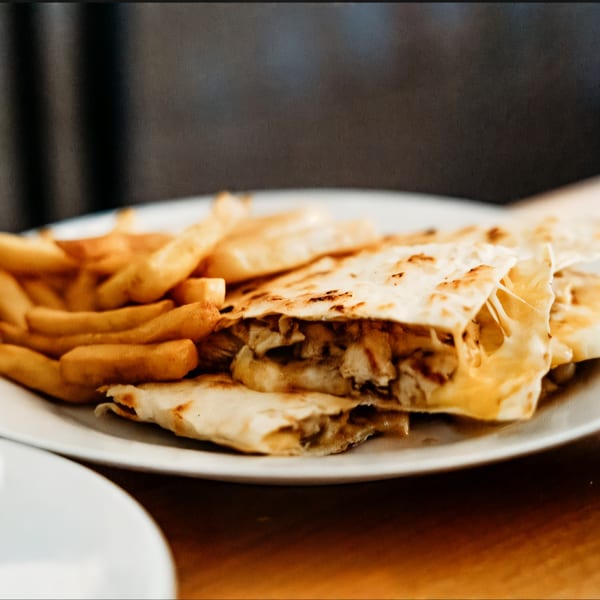 Chicken quesadillas with melted cheese and a side of golden french fries on a white plate.