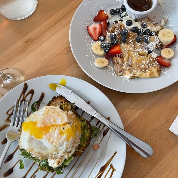 Avocado toast with a fried egg and fruit crepes with syrup on a wooden table.