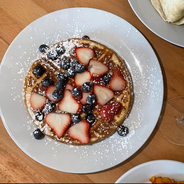 A golden waffle topped with fresh strawberries, blueberries, and powdered sugar on a white plate.