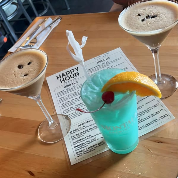 Two espresso martinis and a blue cocktail with orange and cherry garnish on a wooden table.