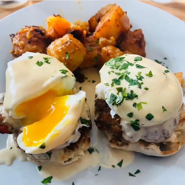 Two eggs benedict with runny yolks and hollandaise sauce, served with roasted potatoes.