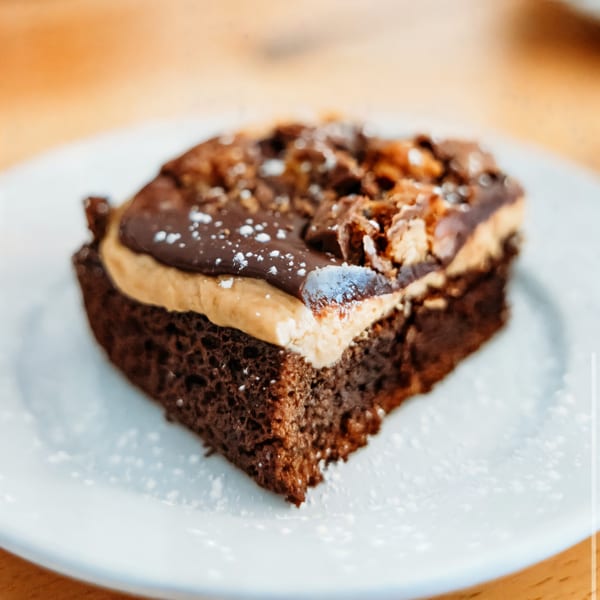A rich chocolate brownie with peanut butter frosting and chocolate drizzle, dusted with powdered sugar.