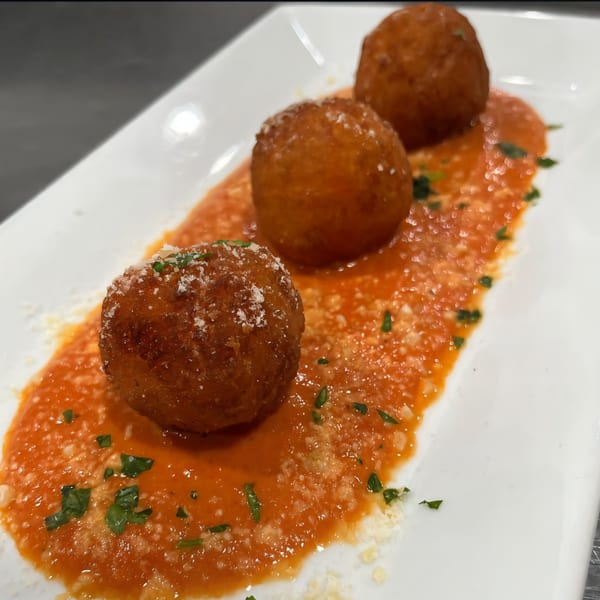 Three golden-brown arancini balls with grated cheese and parsley on a bed of red sauce.