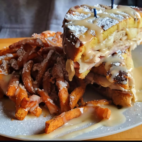 A Monte Cristo sandwich with sweet potato fries, drizzled with sauce and powdered sugar.