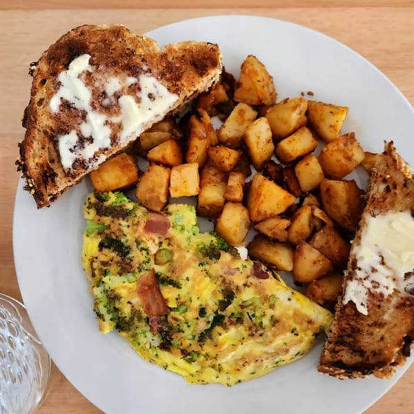 A breakfast plate with a broccoli and ham omelet, home fries, and buttered toast.