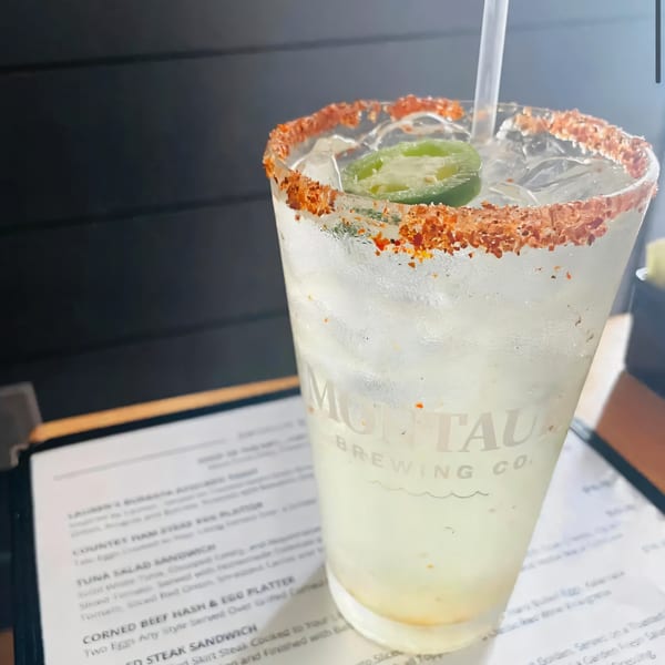 A spicy margarita with a chili-salt rim and jalapeño slices, next to a menu.